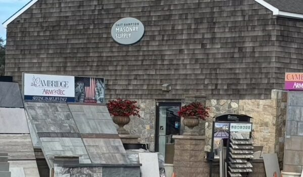 The exterior of East Hampton Masonry Supply, featuring stone siding, a variety of stone slabs on display, and potted flowers near the entrance.