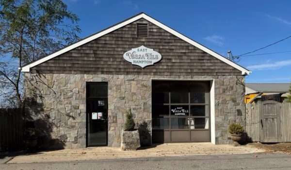 The East Versatile Tile Hampton storefront featuring a stone façade, large windows, and a centered sign under a clear blue sky.